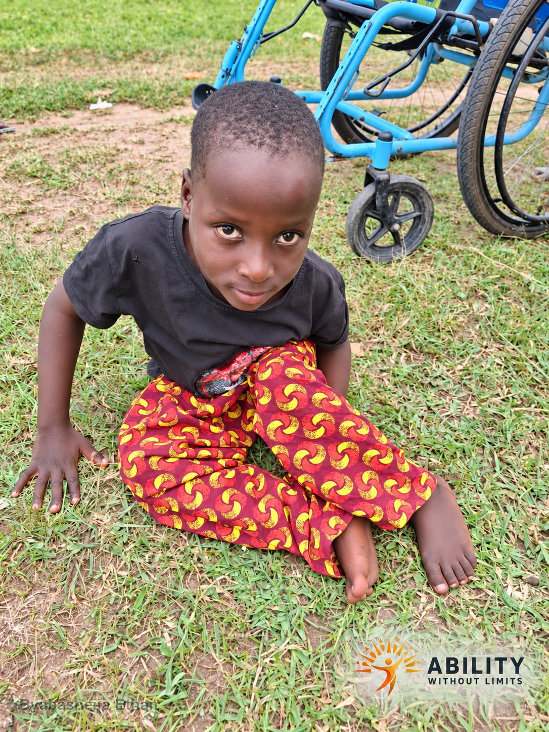 Byabasheija Ethan seated outdoors near a wheelchair